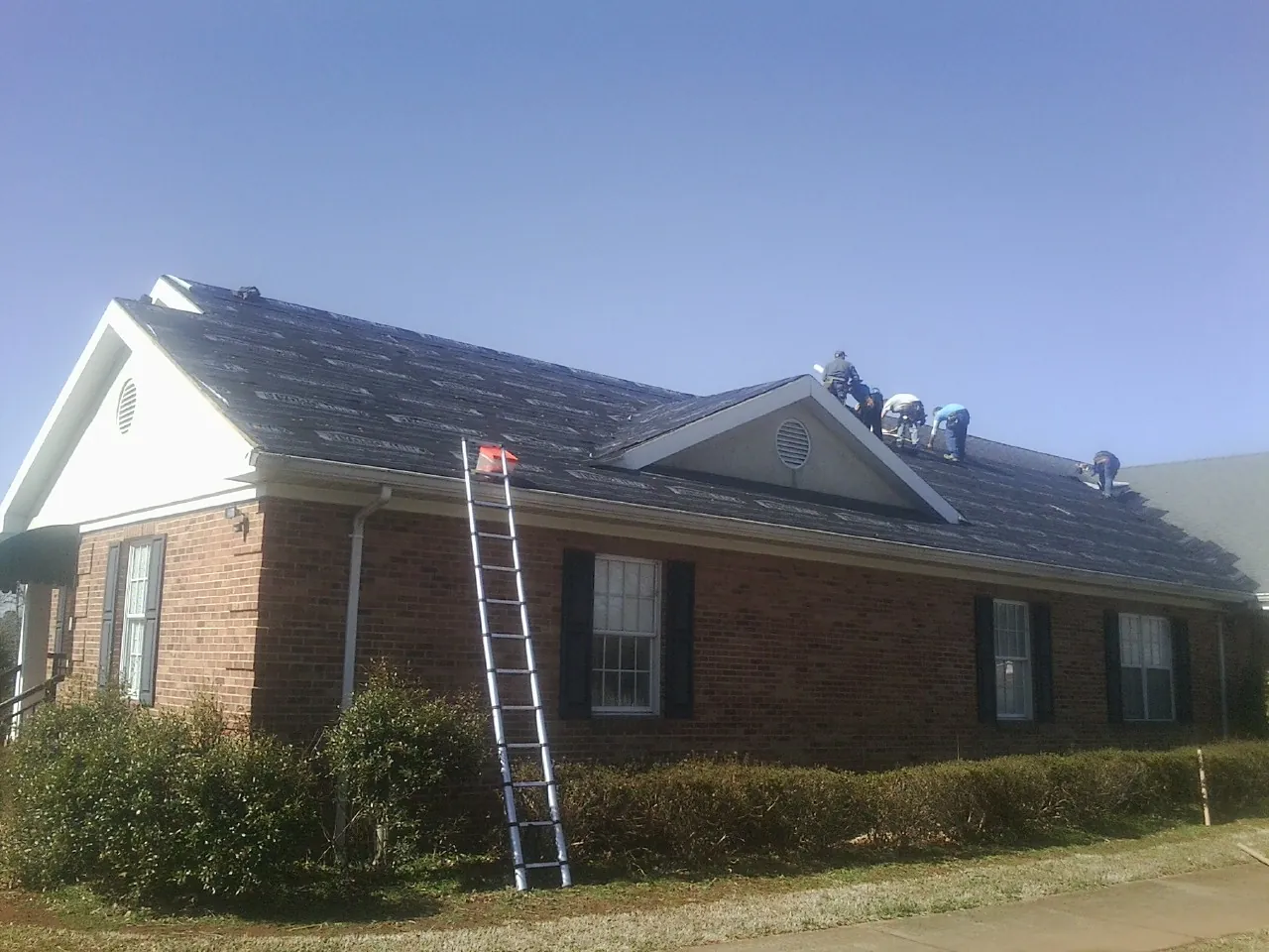 Crew tearing shingles off a brick ranch roof with a ladder set — Emergency Roof Repair work by our crew in Elk River