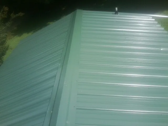 New green metal panels meeting at the ridge of a roof — Flat Roof Repair work by our crew in Elk River