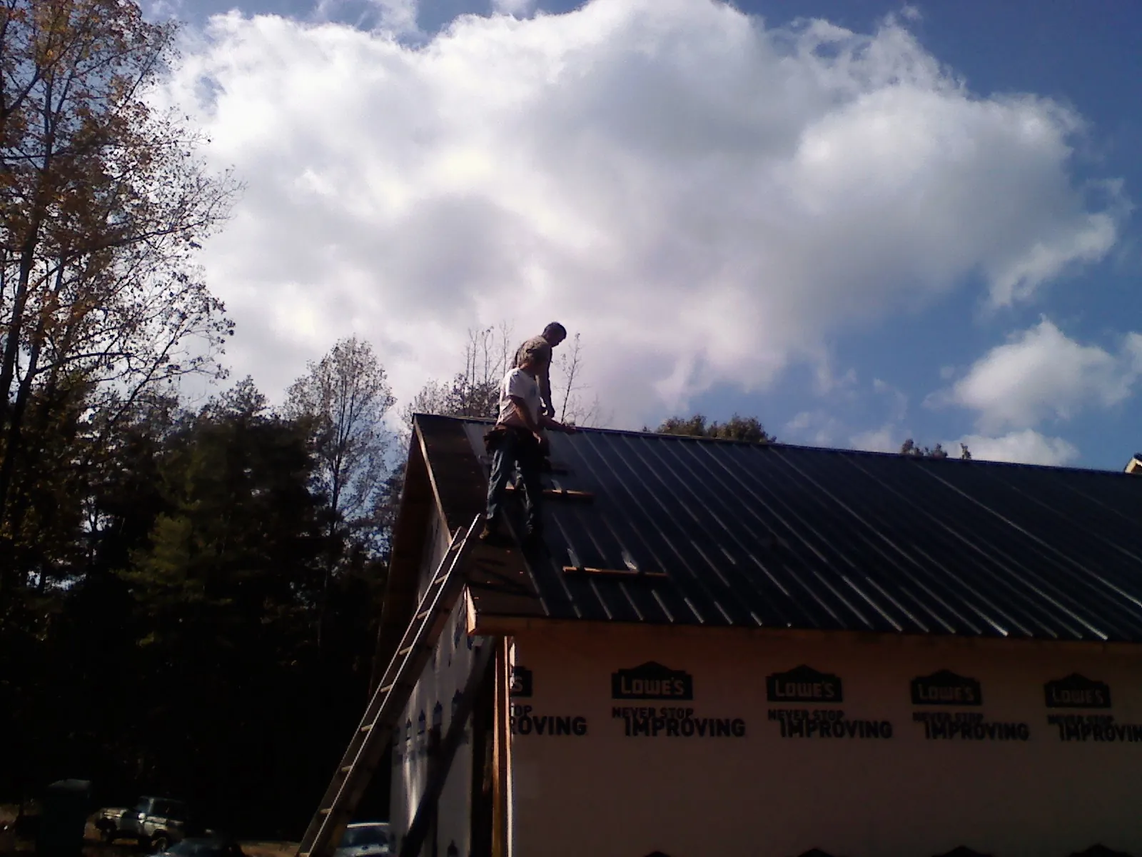 Roofer fastening dark metal panels high against a cloudy sky, from a Roof Inspection job in Elk River