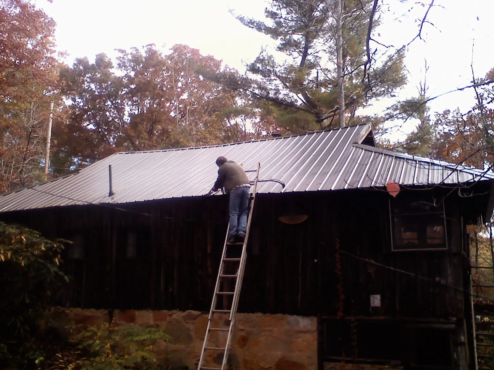 Roofer on a ladder working along the edge of a cabin metal roof in Elk River