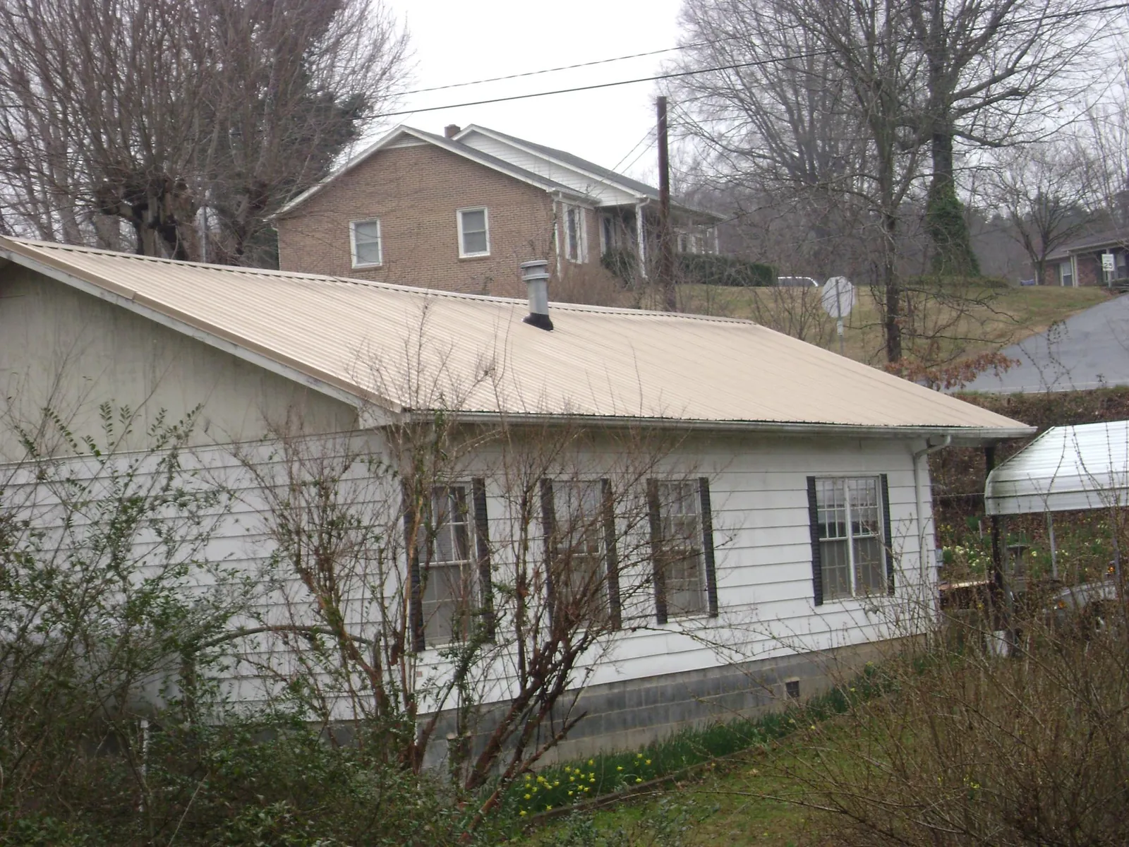 Tan metal roof on a white sided house set into a hillside — Commercial Roofing by Roofing Brothers in Elk River